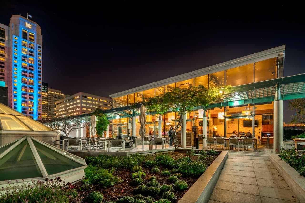 Rooftop promenade at dusk with curved canopy and city skyline lighting